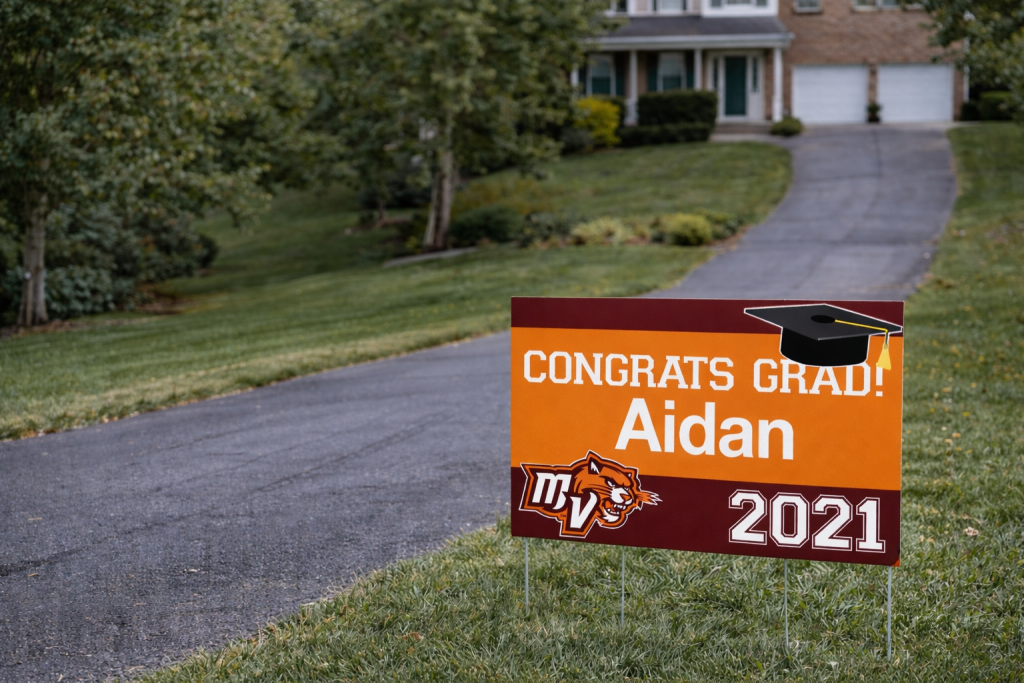 Custom graduation yard sign for Aidan placed beside a residential driveway with bold school colors and graduation year